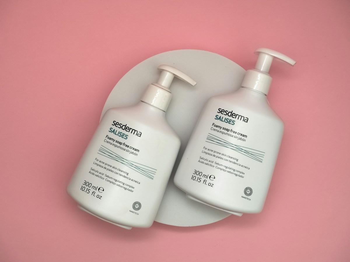 Two pump bottles of face cleanser on a pink background